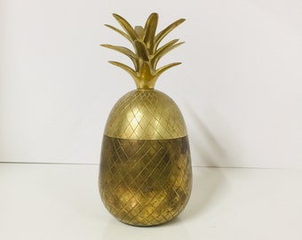 Puede incluir: Un cubo de hielo de forma de piña dorado con una superficie texturizada. La parte superior del cubo es una pieza separada que se asemeja a la parte superior de una piña.