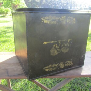 May include: A black metal storage box with a hinged lid. The box has gold painted floral designs on the front and sides.