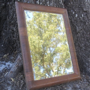 May include: A rectangular mirror with a brown wooden frame. The mirror reflects a green tree with a blue sky in the background.
