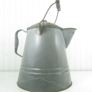May include: A vintage gray enamel camping coffee pot with a wire handle and wooden grip. The pot has a speckled finish and a wide spout.