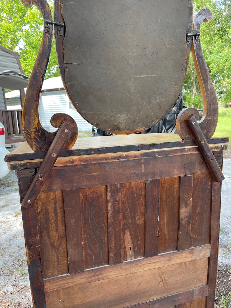 Puede incluir: Espejo de tocador antiguo de madera con un espejo ovalado biselado y un marco de madera tallada ornamentado. El espejo est&aacute; unido a un gabinete de madera con una puerta con bisagras.