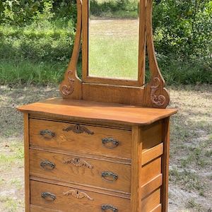 May include: Antique oak dresser with a beveled mirror and three drawers. The dresser has ornate carvings and metal drawer pulls.