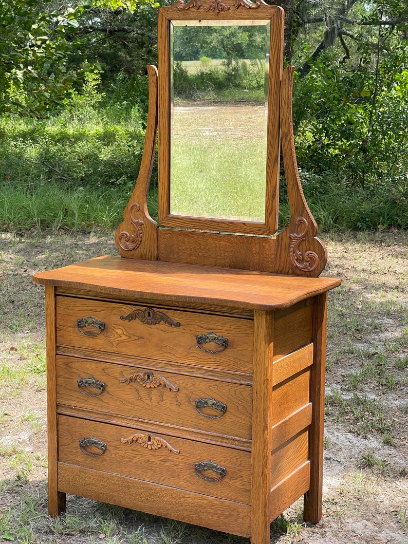 May include: Antique oak dresser with a beveled mirror and three drawers. The dresser has ornate carvings and metal drawer pulls.