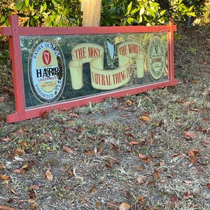 K&ouml;nnte beinhalten: Ein roter, mit Holz gerahmter Spiegel mit einer Harp Lager Beer-Werbung und einer Guinness-Werbung. Der Spiegel tr&auml;gt den Text "The most natural thing in the world".
