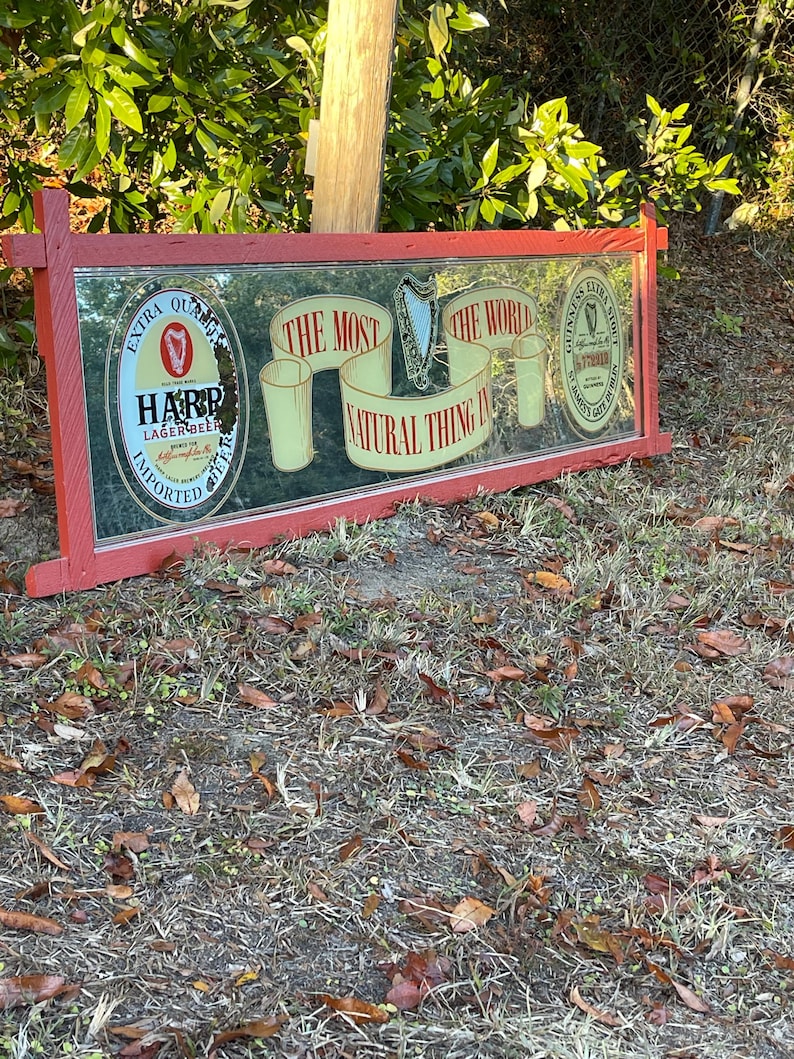 K&ouml;nnte beinhalten: Ein roter, mit Holz gerahmter Spiegel mit einer Harp Lager Beer-Werbung und einer Guinness-Werbung. Der Spiegel tr&auml;gt den Text "The most natural thing in the world".