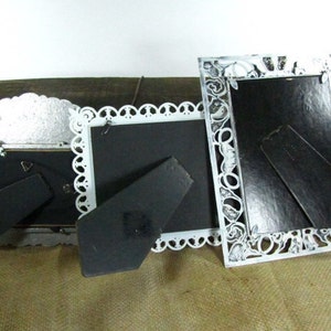 May include: Three ornate white picture frames with black mats and decorative cutouts. The frames are made of metal and have a vintage look.