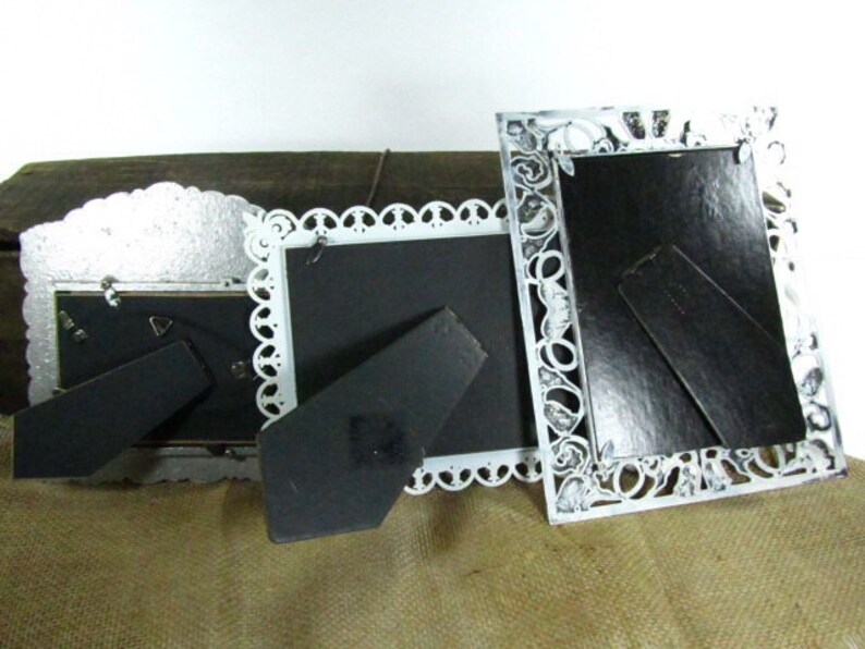 May include: Three ornate white picture frames with black mats and decorative cutouts. The frames are made of metal and have a vintage look.