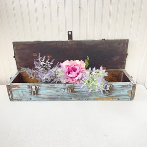May include: A light blue wooden box with two metal clasps and a distressed finish. The box is open and contains a bouquet of pink and purple flowers.