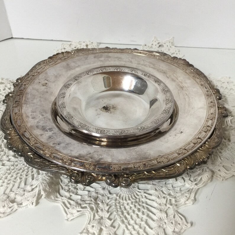 Puede incluir: Un plato de servir de plata con un taz&oacute;n m&aacute;s peque&ntilde;o en el centro. El plato tiene un borde decorativo festoneado y dise&ntilde;os florales intrincados.