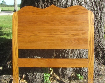May include: A wooden headboard with a curved top and a horizontal slat. The headboard is made of light brown wood with a natural wood grain.
