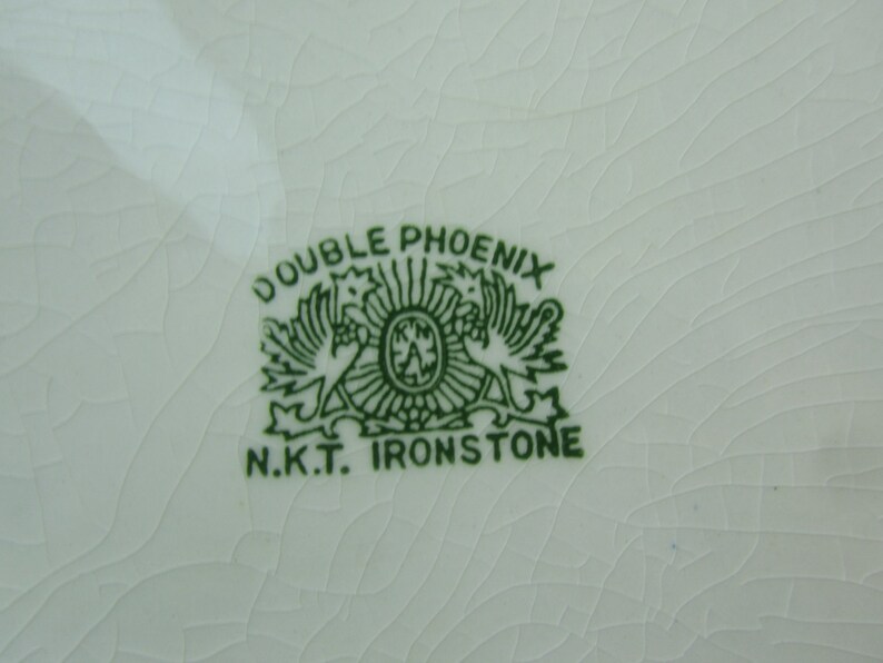 K&ouml;nnte beinhalten: Gr&uuml;nes und wei&szlig;es Double Phoenix N.K.T. Ironstone Logo mit zwei sich gegen&uuml;berstehenden Ph&ouml;nixv&ouml;geln.