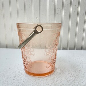 May include: A pink glass ice bucket with a silver handle. The bucket features a delicate floral pattern etched into the glass.