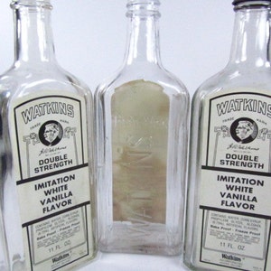 May include: Three clear glass bottles with white labels. The labels have black text that reads "Watkins", "Trade Mark", "Double Strength", "Imitation White Vanilla Flavor", and "11 Fl. Oz".
