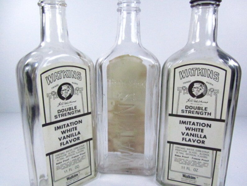 May include: Three clear glass bottles with white labels. The labels have black text that reads "Watkins", "Trade Mark", "Double Strength", "Imitation White Vanilla Flavor", and "11 Fl. Oz".