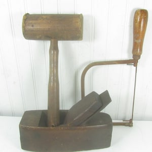 May include: A vintage wooden mallet with a metal blade and a wooden handle. The mallet is attached to a wooden base with a metal saw blade.