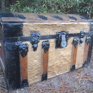 May include: Antique wooden trunk with a crocodile-embossed leather finish. The trunk has black metal accents, including a lock and hinges. The trunk is in good condition and has a vintage look.