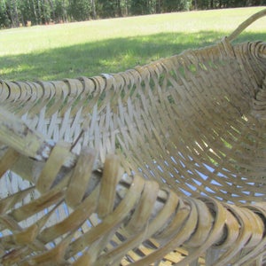 May include: A woven basket made of natural materials, with a light brown color and a woven pattern. The basket has a handle and is shaped like a half-circle.
