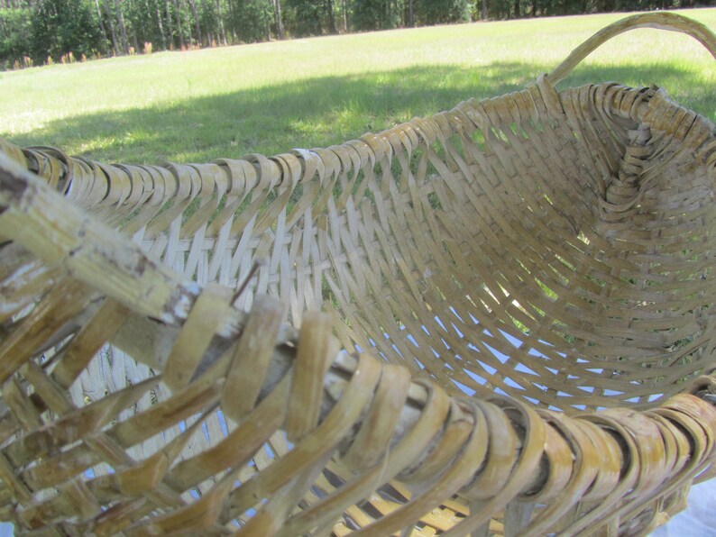 May include: A woven basket made of natural materials, with a light brown color and a woven pattern. The basket has a handle and is shaped like a half-circle.