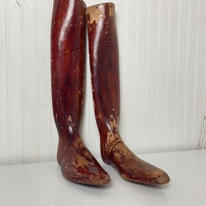 May include: A pair of antique wooden boot forms. The forms are made of wood and have a reddish-brown color. They are slightly worn and have a distressed look.