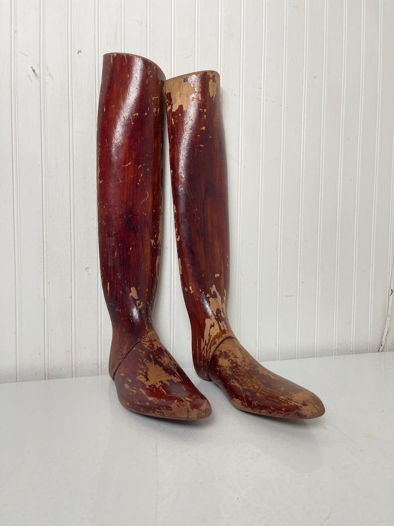 May include: A pair of antique wooden boot forms. The forms are made of wood and have a reddish-brown color. They are slightly worn and have a distressed look.
