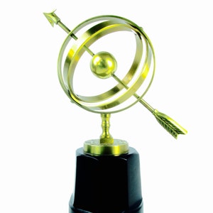May include: A gold-colored metal sculpture of a globe with an arrow piercing through it. The globe is on a black base.