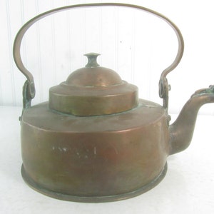 Puede incluir: Tetera de cobre antigua con un asa curva y un pico en forma de cabeza de pájaro. La tetera tiene una tapa con un pomo en la parte superior.