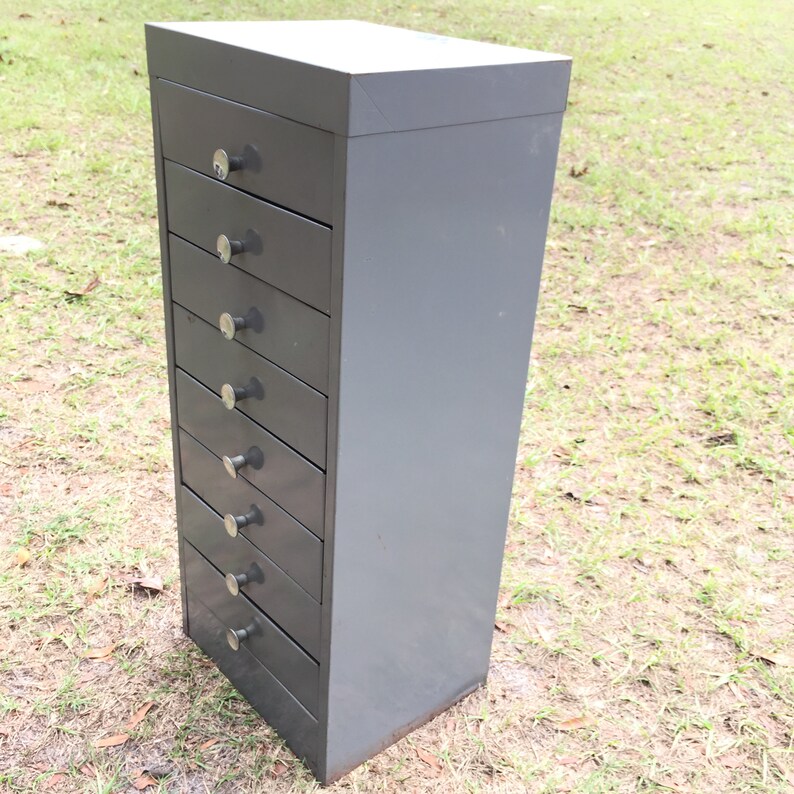 May include: A gray metal cabinet with eight drawers. Each drawer has a silver knob.