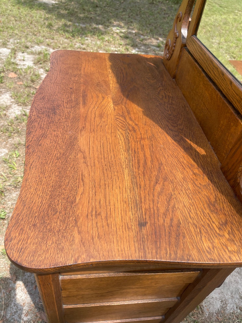 May include: A vintage wooden vanity with a curved top and three drawers. The vanity is made of dark wood with a rich brown finish. The vanity has a mirror on the top, which is not visible in the image.