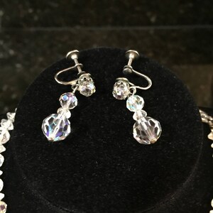 May include: A pair of silver clip-on earrings with clear crystal beads. The earrings have a dangling design with three beads on each earring.