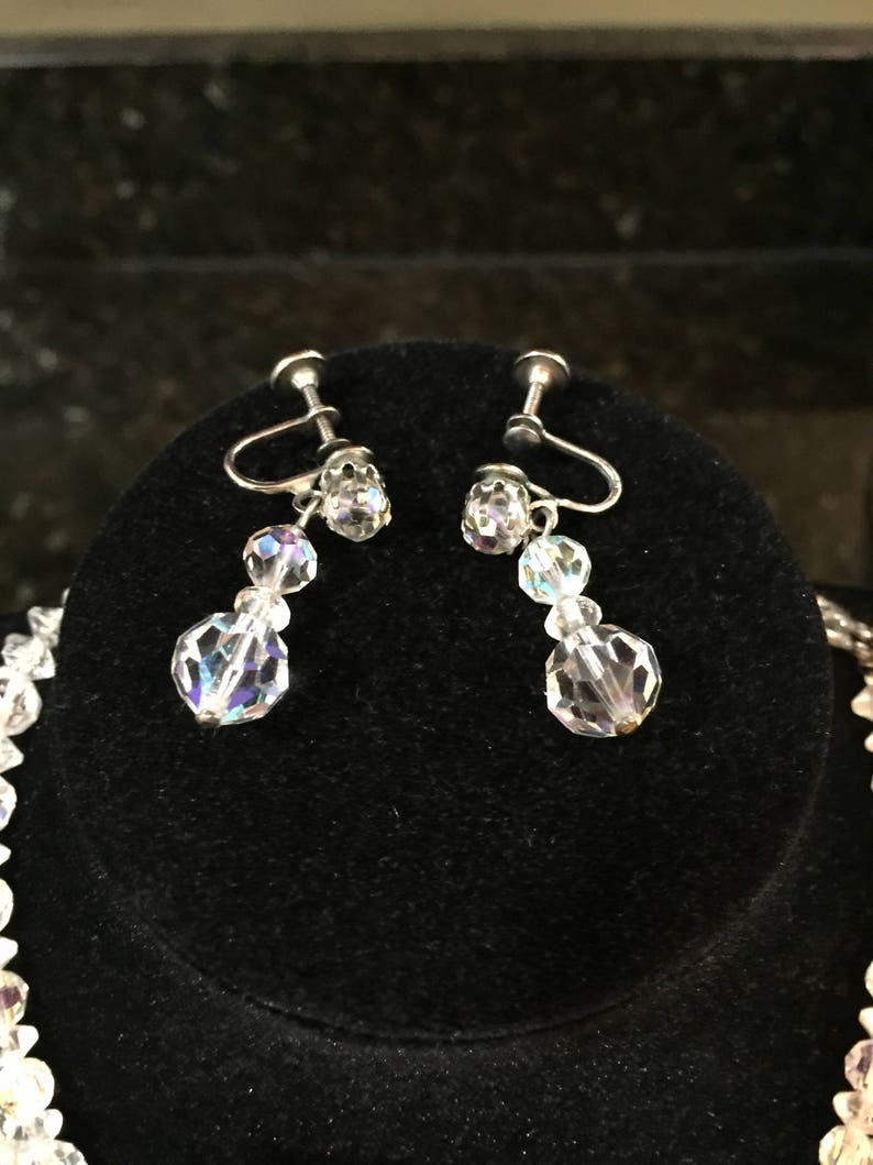 May include: A pair of silver clip-on earrings with clear crystal beads. The earrings have a dangling design with three beads on each earring.