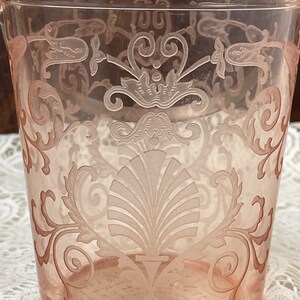 May include: A pink glass ice bucket with an etched floral design. The design features a large shell in the centre and smaller floral motifs around the edges.