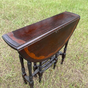 May include: A dark wood drop leaf table with a rounded top and intricate carved legs. The table is in a folded position and has a dark brown finish.