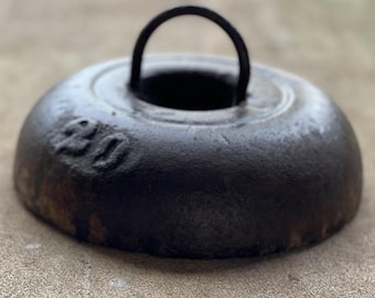 Puede incluir: Un peso de hierro fundido negro con un asa de anillo de metal. El peso es redondo y tiene el número "20" grabado en el lateral.