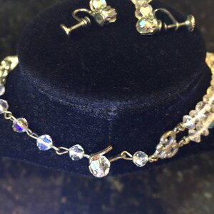 May include: A crystal necklace and earrings set with a silver chain and clear crystal beads. The necklace has a clasp closure. The earrings are clip-on style.