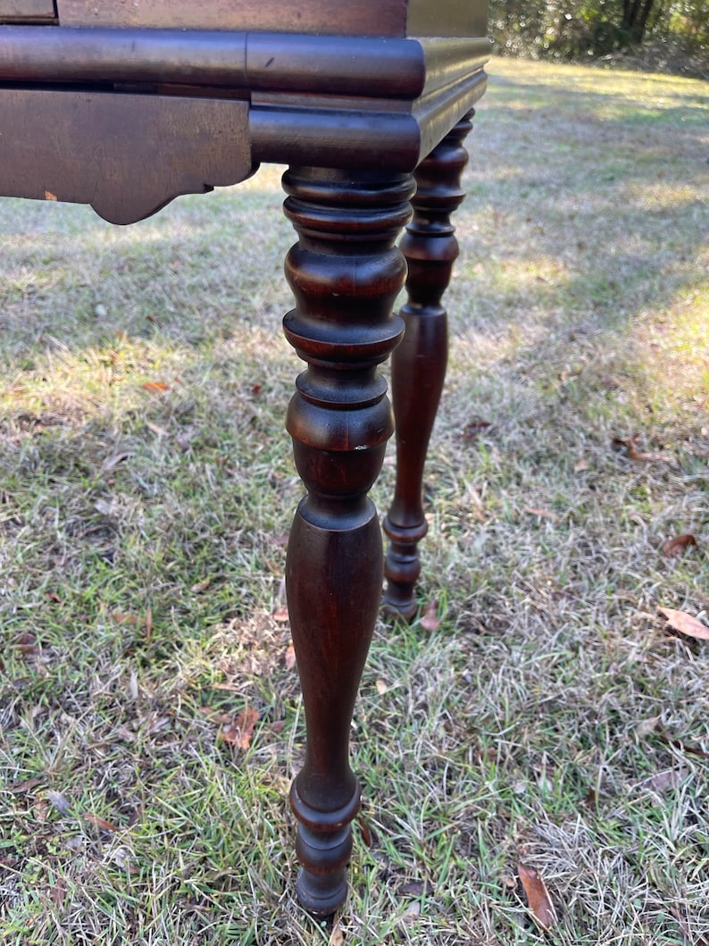 May include: Close-up of the turned legs of a dark brown wooden table. The legs are round and have a decorative design.