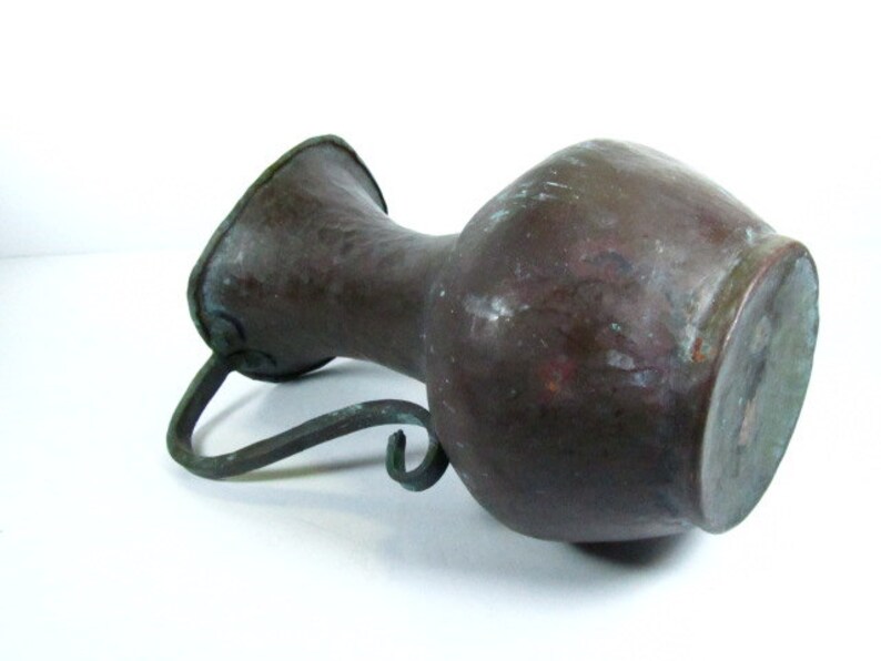 K&ouml;nnte beinhalten: Eine antike Kupferkanne mit geh&auml;mmerter Oberfl&auml;che und einem gebogenen Eisenhenkel. Die Kanne hat eine dunkelbraune Patina und ist in gutem Zustand.