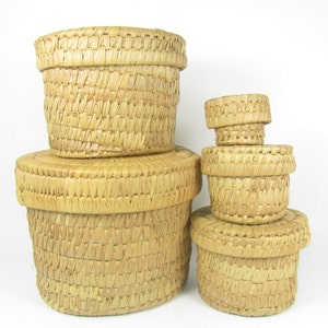 May include: Set of five woven straw baskets in various sizes, stacked on top of each other. The baskets are a light brown color and have a natural, rustic look.