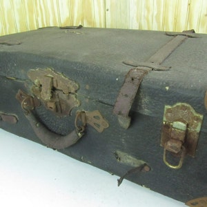 May include: A vintage, dark brown leather suitcase with metal hardware and a leather handle. The suitcase has a worn and weathered look, with signs of age and use.