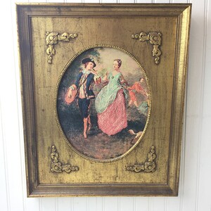May include: A framed oval print of a painting depicting a couple in 18th century clothing in a garden setting. The frame is gold with ornate details.
