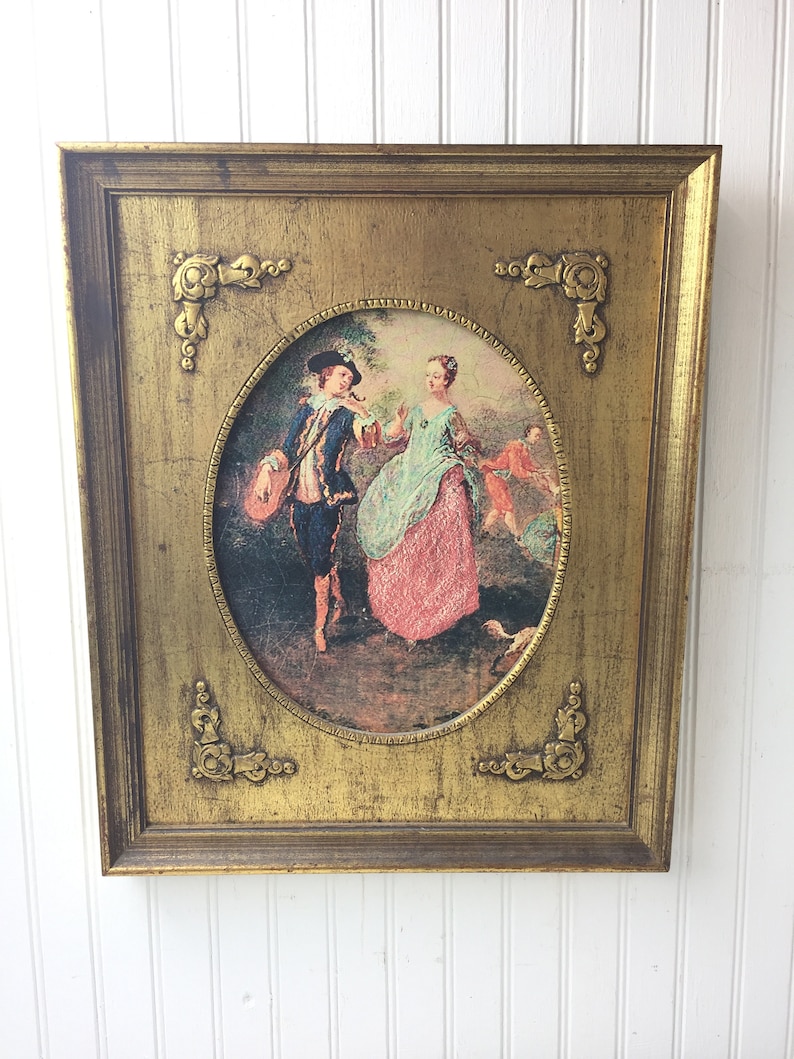 May include: A framed oval print of a painting depicting a couple in 18th century clothing in a garden setting. The frame is gold with ornate details.