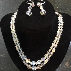 May include: A two-strand crystal necklace and matching earrings. The necklace is made of clear faceted beads and the earrings are teardrop shaped with a single crystal bead.