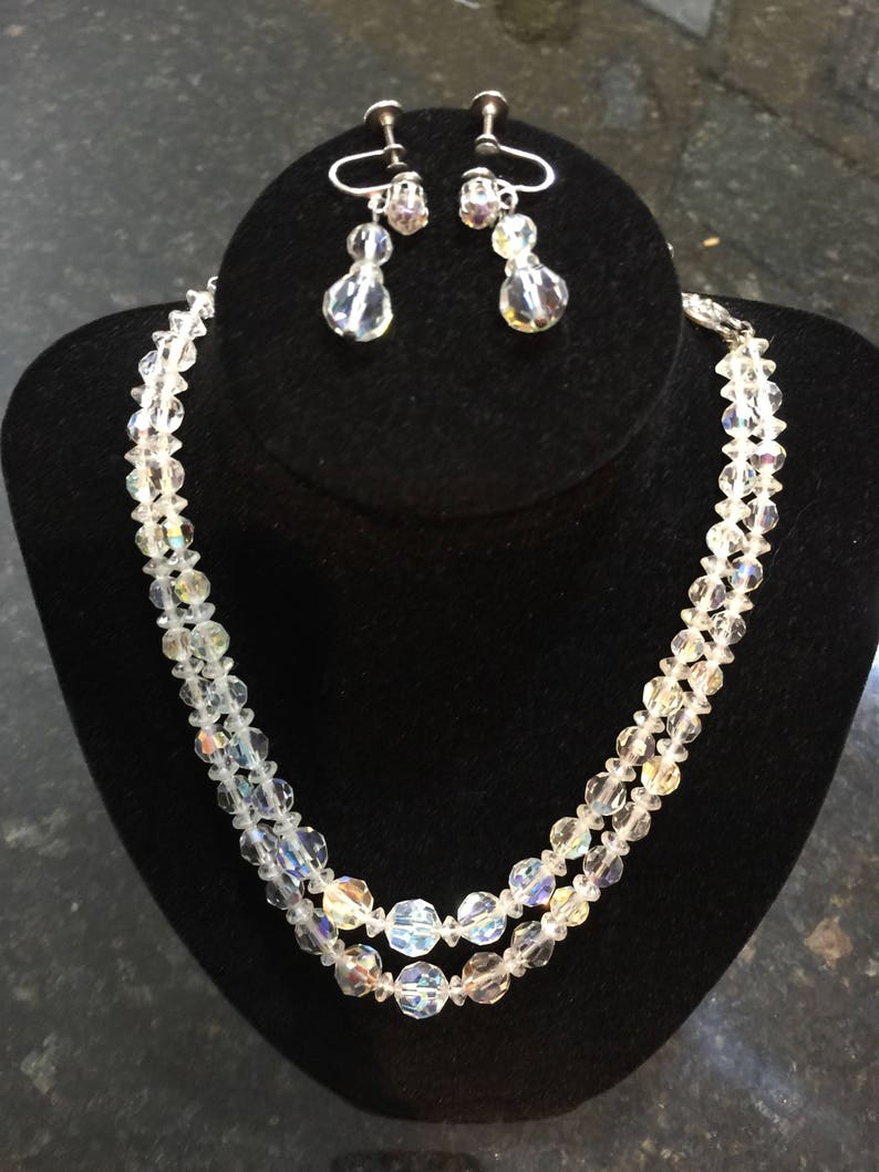 May include: A two-strand crystal necklace and matching earrings. The necklace is made of clear faceted beads and the earrings are teardrop shaped with a single crystal bead.