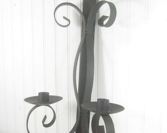 May include: Black metal wall-mounted candle holder with two candle holders and a scrolled design.