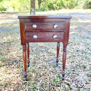 May include: A dark brown wooden end table with two drawers and turned legs. The table has silver-toned drawer pulls.