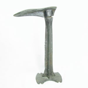 May include: A vintage cast iron shoe last, a tool used by shoemakers to shape and stretch leather. The last is made of metal and has a long, slender shaft with a curved foot at the top.