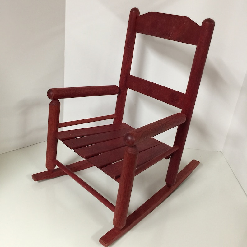 Puede incluir: Una silla mecedora de madera roja con un asiento de listones y un respaldo alto. La silla est&aacute; hecha de madera maciza y tiene un estilo r&uacute;stico, de granja.