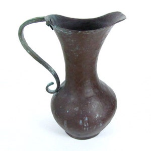 K&ouml;nnte beinhalten: Ein antiker Kupferkrug mit geh&auml;mmerter Oberfl&auml;che und einem dekorativen Schmiedeeisenhenkel. Der Krug hat eine dunkelbraune Patina und ist in gutem Zustand.
