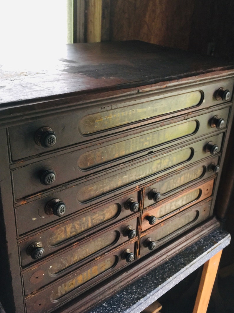 May include: A dark brown wooden cabinet with eight drawers. Each drawer has a glass front with faded labels. The cabinet has black knobs on each drawer.