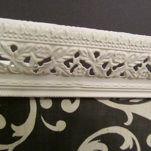Puede incluir: Bandeja de metal blanco con un dise&ntilde;o floral decorativo alrededor del borde. La bandeja est&aacute; sobre una superficie con un patr&oacute;n blanco y negro.