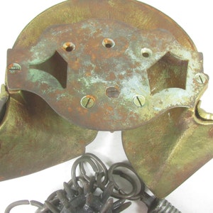 May include: A vintage brass door knocker with a decorative design. The knocker is in two pieces, with a hinged top and a bottom piece that swings open. The knocker is attached to a chain with a ring at the end.